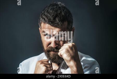 Primo piano ritratto di un serio uomo di karate in kimono bianco. Maestro di arti marziali in posizione di combattimento. Lottatore di karate in preparazione alla competizione. Forte Foto Stock