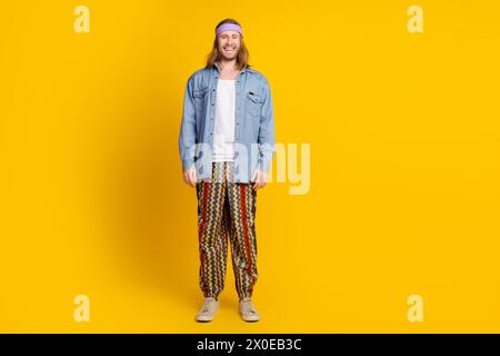 Foto a tutto il corpo di un giovane uomo hippie che posa il modello indossa abiti di tendenza in denim isolati su sfondo giallo Foto Stock