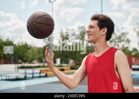 Un giovane giocatore di basket con una maglia rossa che lancia un pallacanestro all'aperto in una giornata di sole. Foto Stock