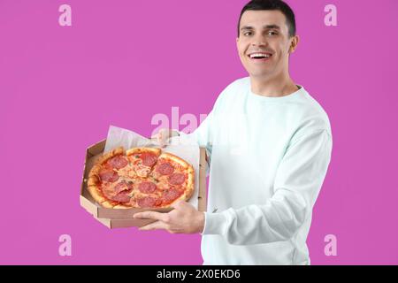 Giovane con gustosa pizza al peperoni su sfondo viola Foto Stock