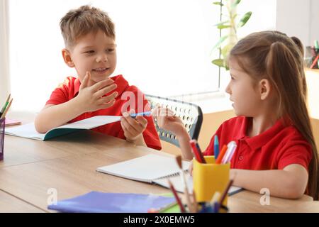 Piccoli allievi carini che scrivono a tavola in classe. Concetto di vacanze scolastiche Foto Stock