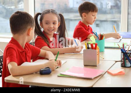 Piccoli allievi carini che scrivono a tavola in classe. Concetto di vacanze scolastiche Foto Stock