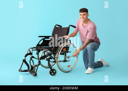 Bellissimo giovane uomo felice con chiave che ripara sedia a rotelle su sfondo blu Foto Stock