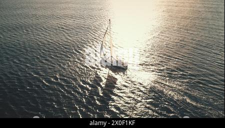 Riflesso del sole sullo yacht che naviga sull'antenna della baia cristallina del mare. Mesmerezing Seacape con barca a vela in estate, giorno di luce solare intensa. Tranquillo lungomare con barca a vela da sola al soffio del vento al colpo del drone Foto Stock