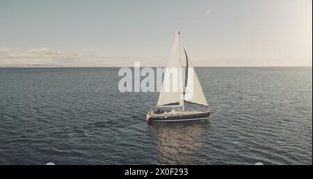 Prendi il sole nella baia dell'oceano con l'antenna di uno yacht di lusso. Nessuno può ammirare la natura durante la crociera estiva alla luce del sole. Barca a vela in mare aperto. Veliero bianco sull'acqua al cinema con un drone. Concetto di viaggio e turismo Foto Stock