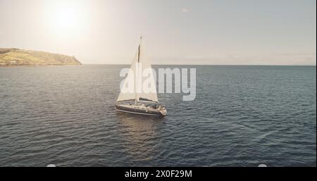 Prendi il sole nella baia dell'oceano con l'antenna di uno yacht di lusso. Nessuno può ammirare la natura durante la crociera estiva alla luce del sole. Barca a vela in mare aperto. Veliero bianco sull'acqua al cinema con un drone. Concetto di viaggio e turismo Foto Stock