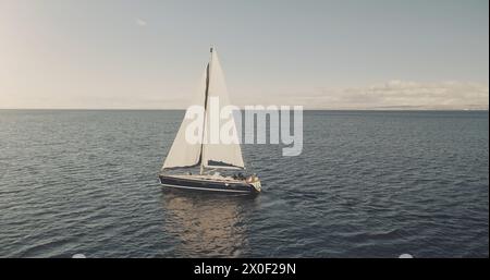 Prendi il sole nella baia dell'oceano con l'antenna di uno yacht di lusso. Nessuno può ammirare la natura durante la crociera estiva alla luce del sole. Barca a vela in mare aperto. Veliero bianco sull'acqua al cinema con un drone. Concetto di viaggio e turismo Foto Stock