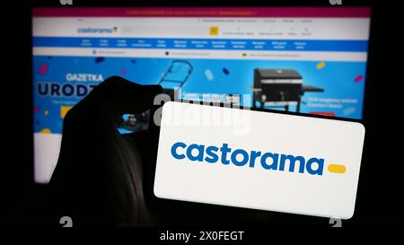 Persona che detiene un telefono cellulare con il logo della catena di negozi di articoli per il miglioramento della casa Castorama davanti alla pagina Web aziendale. Mettere a fuoco il display del telefono. Foto Stock