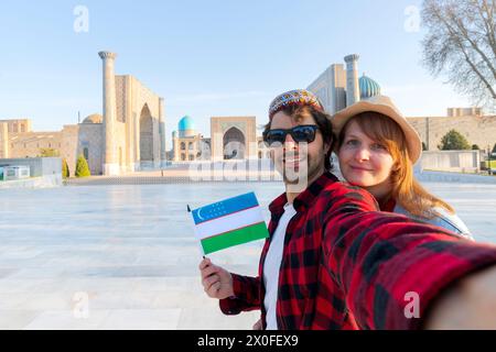 Coppia felice di turisti che fanno un selfie con Registan come sfondo nella città di Samarcanda, Uzbekistan, Asia centrale Foto Stock