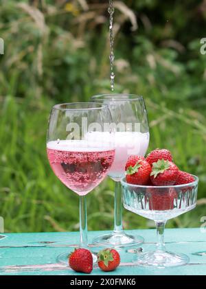 Due bicchieri di vino frizzante rosa e fragola su un tavolo. Picnic romantico all'aperto. Foto ravvicinata di stoviglie in vetro. Cibo e bevande estive. Foto Stock