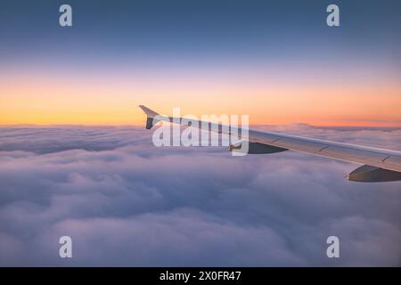 Aereo che vola sopra le nuvole di cielo colorato durante il tramonto panoramico o il paesaggio dell'alba, vista dalla finestra dell'aereo delle turbine ad ala e dell'orizzonte Foto Stock
