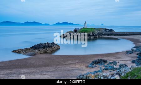 La spiaggia di Ynys Llanddwyn, una piccola isola di marea al largo della costa occidentale di Anglesey. È ora blu e il mare è calmo, con montagne dietro Foto Stock