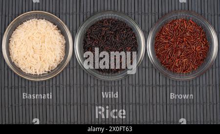 Tre ciotole trasparenti mostrano diverse varietà di riso: Basmati, Wild e Brown. L'assortimento rappresenta diversi tipi di cereali utilizzati in cu internazionale Foto Stock