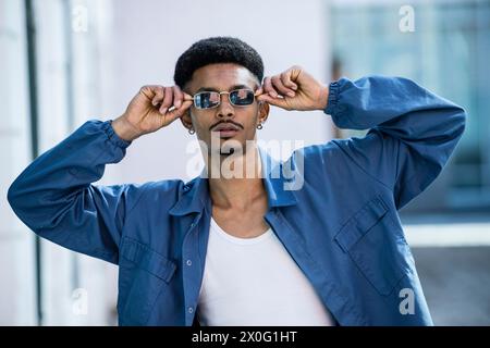 Elegante giovane adulto con occhiali da sole che guarda la macchina fotografica all'esterno. Foto Stock