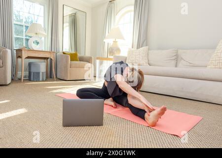 Lo yoga si allunga in un elegante soggiorno illuminato dal sole Foto Stock