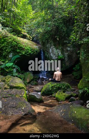 Uomo adulto che fa il bagno sulla cascata all'ingresso della grotta nella verde foresta atlantica Foto Stock