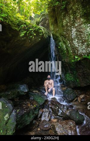 Uomo adulto che fa il bagno sulla cascata all'ingresso della grotta nella verde foresta atlantica Foto Stock