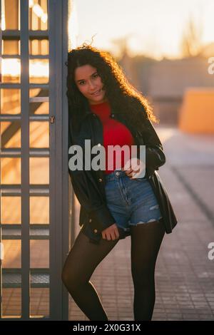 Giovane donna appoggiata su una recinzione di metallo al tramonto Foto Stock