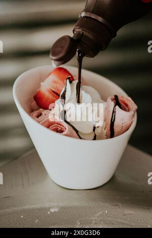 Il cioccolato è stato versato sul gelato arrotolato alla fragola e sulla panna montata Foto Stock