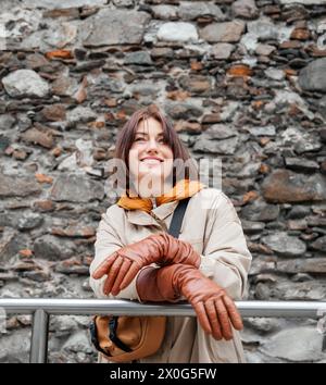 Donna contemplativa appoggiata su ringhiera contro muro di pietra Foto Stock