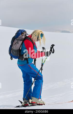 Uno sciatore determinato scala una vetta innevata nelle Alpi, portando con sé l'attrezzatura da backcountry per una discesa epica. Foto Stock