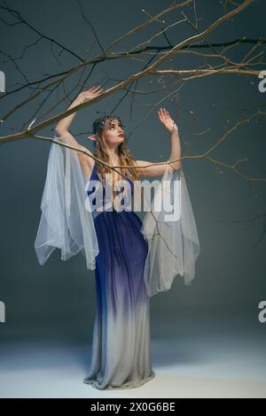 Una giovane donna vestita di blu e bianco ha un ramo delicato, incarnando una principessa fatata in un ambiente stravagante. Foto Stock