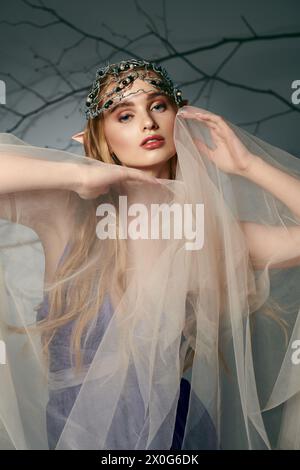 Una giovane donna, vestita come una principessa elfa da favola, si erge con un velo graziosamente drappeggiato sulla sua testa. Foto Stock