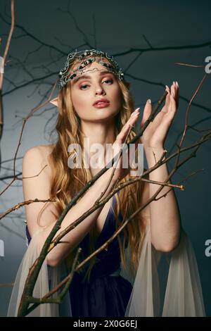Una giovane donna incoronata in una maestosa corona, vestita con un bellissimo abito blu, trasuda l'essenza di una principessa fatata in un ambiente studio. Foto Stock