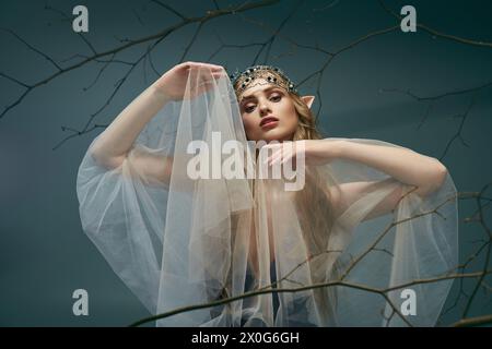 Una giovane donna, vestita da principessa elfica, si erge con un velo che adorna la sua testa in un mistico ambiente studio. Foto Stock