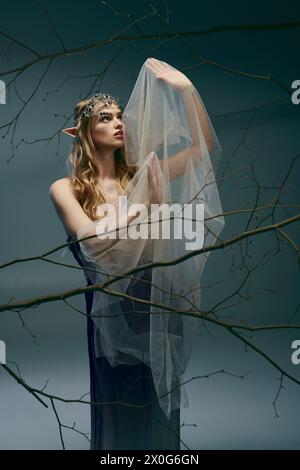 Una giovane donna vestita da principessa elfica si erge graziosamente di fronte a un maestoso albero che indossa un velo. Foto Stock