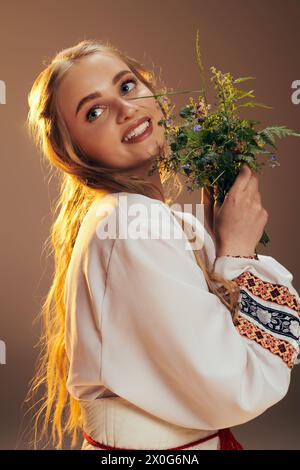 Un giovane mavka in abito bianco regala graziosamente un bouquet di fiori in un ambiente fantastico da studio. Foto Stock