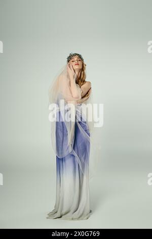 Una giovane donna vestita con un abito blu e bianco con un velo che scorre, incarnando l'essenza di una principessa fatata in un ambiente studio. Foto Stock