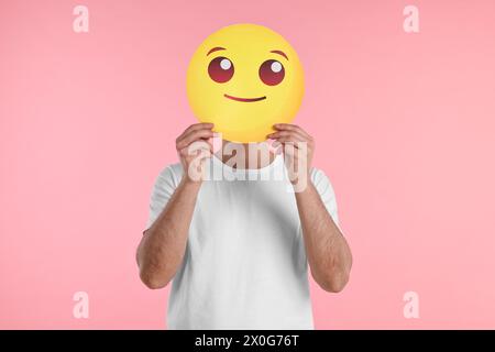 Uomo che copre il viso con emoticon sorridente su sfondo rosa Foto Stock