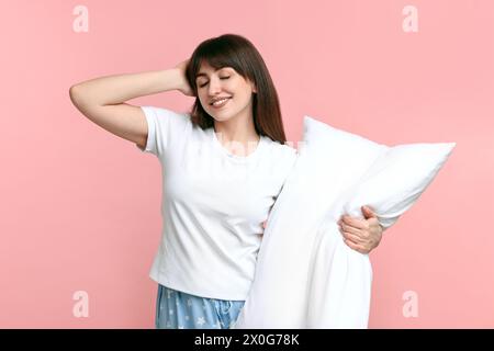 Donna felice in pigiama che regge il cuscino su sfondo rosa Foto Stock