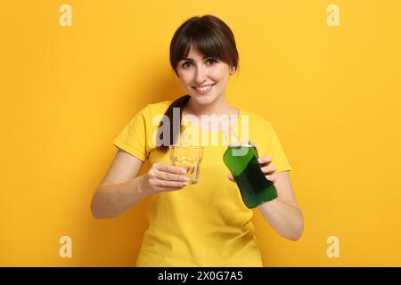 Giovane donna che usa collutorio su sfondo giallo Foto Stock