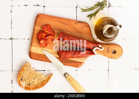 Chorizo iberico, chorizo spagnolo ​​or salsiccia spagnola tagliata a fette su una tavola di legno con pane rustico. Sfondo piastrelle bianche. Copia spazio. Foto Stock