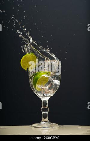 Il limone cade in un bicchiere d'acqua trasparente causando schizzi verso l'alto. Foto Stock