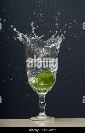 Il limone cade in un bicchiere d'acqua trasparente causando schizzi verso l'alto. Foto Stock