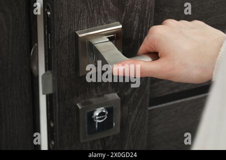 Donna che apre una porta di legno in interni, primo piano della mano sulla maniglia Foto Stock