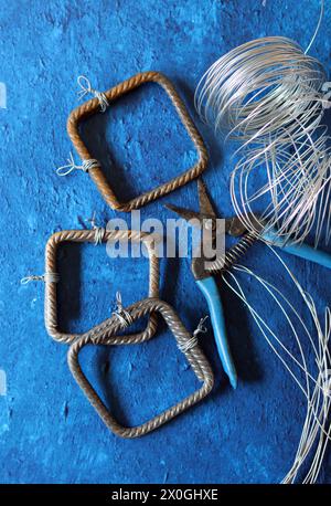 Pinze vintage, filo e acciaio di rinforzo su sfondo blu testurizzato con spazio di copia. Lavori di ristrutturazione della casa nei dettagli. Foto Stock