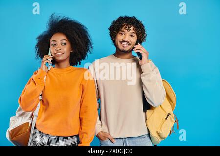Un uomo e una donna interrazziali stanno uno accanto all'altro in uno studio, parlando su smartphone, mostrando diversità e unità. Foto Stock