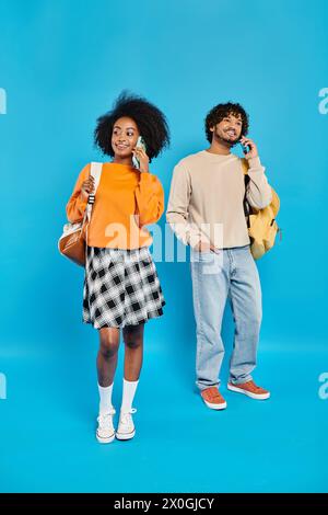 Una coppia interrazziale di studenti con abbigliamento casual si staglia insieme su uno sfondo blu in uno studio. Foto Stock