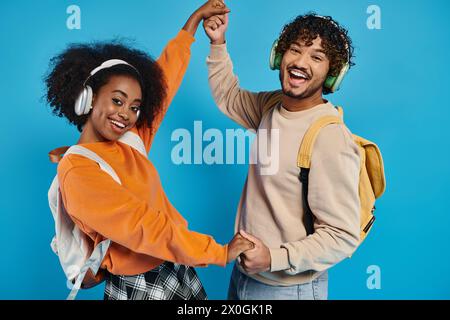 Un uomo e una donna interrazziali ballano insieme, indossando le cuffie, esprimendo gioia e connessione attraverso il movimento su uno sfondo blu. Foto Stock