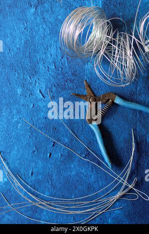 Pinze vintage, filo e acciaio di rinforzo su sfondo blu testurizzato con spazio di copia. Lavori di ristrutturazione della casa nei dettagli. Foto Stock