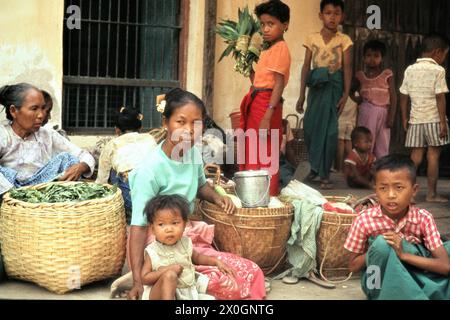 Una famiglia birmana con prodotti in vendita è in attesa per l'autobus su una strada a Bagan. [traduzione automatica] Foto Stock