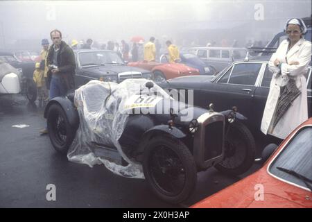 Un'auto coperta di lamina di nylon in nebbia su un parcheggio al Nürburgring durante i preparativi per il Gran Premio Oldtimer dell'Automobile Club di Germania. [traduzione automatica] Foto Stock