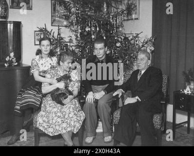 Una famiglia è seduta di fronte all'albero di Natale decorato. [traduzione automatica] Foto Stock