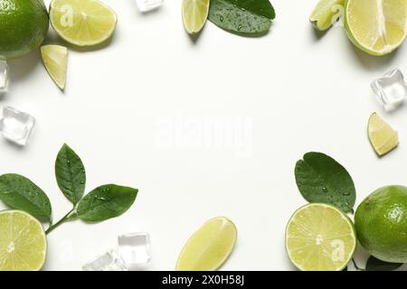 Cornice realizzata in lime maturi con foglie verdi e cubetti di ghiaccio su sfondo bianco, piano Foto Stock