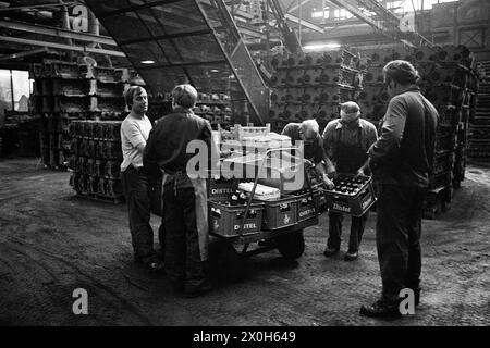 Un gruppo di lavoratori dello stabilimento Mercedes-Benz di Mannheim si riuniscono intorno a un carrello per bevande. I prodotti lattiero-caseari e la birra sono in vendita al carrello durante la pausa. I blocchi motore sono impilati sullo sfondo. [traduzione automatizzata] Foto Stock