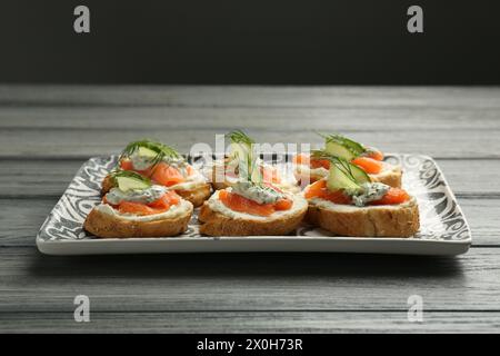 Stuzzichini gustosi con salmone, cetriolo, formaggio spalmabile e aneto su un tavolo di legno Foto Stock